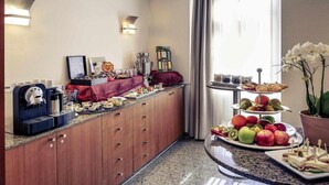 Een hotelkamer met kitchenette, koffieapparaat, fruitplateau en etagère voor desserts.