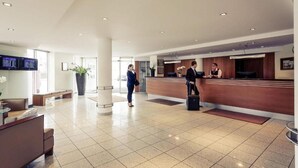 Een hotellobby met een receptiebalie, een zithoek en een grote kamerplant.