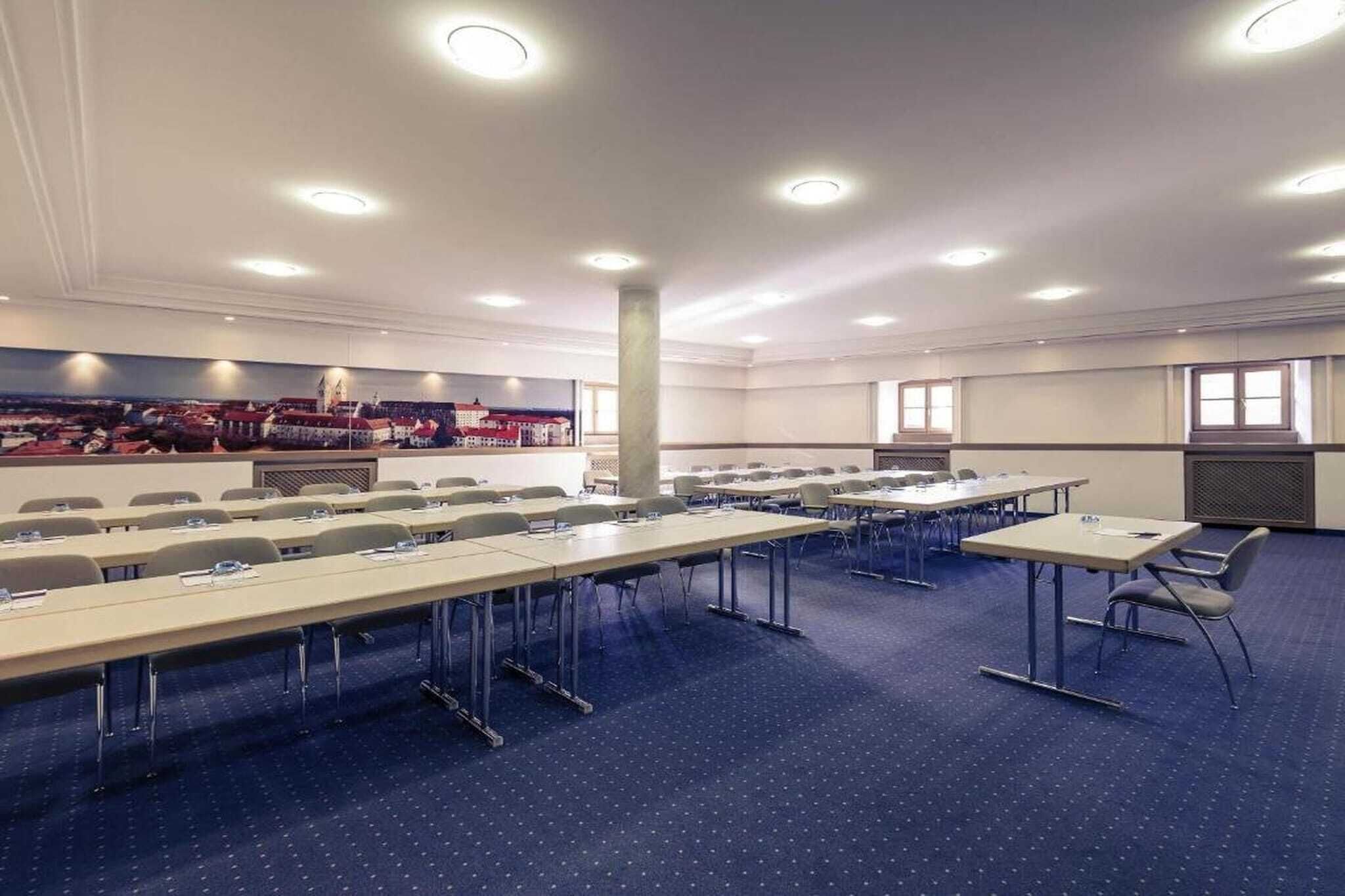 A conference room with multiple tables and chairs, a large pillar, and a cityscape mural on the wall.