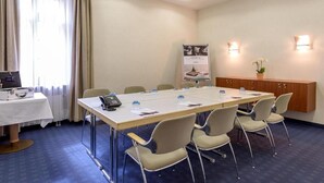 Ein Konferenzraum mit langem Tisch, sechs Stühlen, einem Rednerpult, einem Wasserspender und einem Plakat an der Wand.