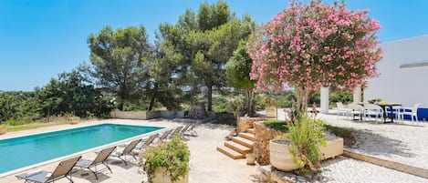 Un área de piscina con sillones reclinables, un muro de piedra y un árbol de flores rosadas.