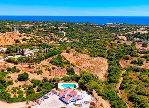 An aerial view of a coastal property with a swimming pool, multiple buildings, and surrounding greenery.