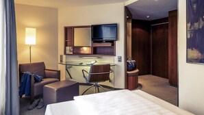 Habitación de hotel con cama, escritorio con silla, televisor, lámpara y armario.