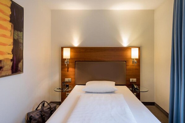 A hotel room with a large bed, two bedside tables, a wooden headboard, and two wall-mounted lamps. - Sunday Hotel München Airport Freising Superior Single Room (Freising)