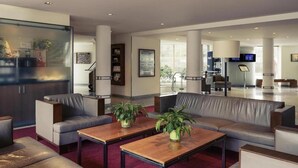Un moderno vestíbulo de hotel con sofás de cuero, mesas de madera y plantas en macetas.