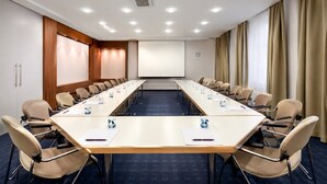 Un salón de conferencias con una larga mesa, sillas, una pantalla de proyector y un reloj en la pared.