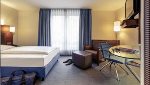 Una habitación de hotel con una cama, un escritorio, una silla, una mesita y un televisor.
