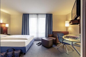 Ein Hotelzimmer mit einem Bett, einem Schreibtisch, einem Sessel, einem kleinen Tisch und einem Fernseher.