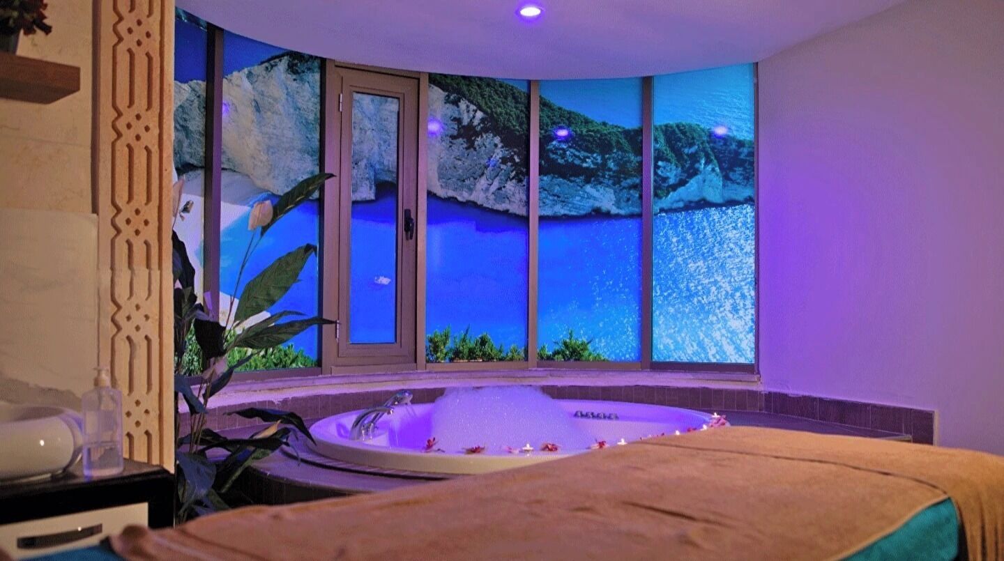 Un cuarto de spa con una bañera grande, una camilla de masaje y vistas panorámicas a través de las ventanas.