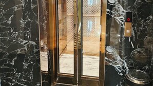 An elevator with a glass door and a fire alarm switch on the wall. - Hotel Varanasi Ganges (Varanasi)