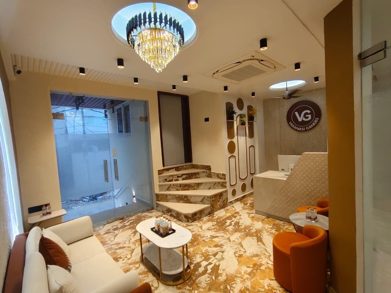 A modern hotel lobby with a chandelier, marble flooring, a reception desk, and seating areas.