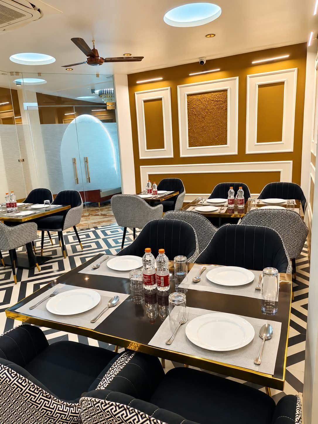 Una sala da pranzo di un hotel con tavoli apparecchiati per quattro persone, completa di piatti, posate e bottiglie d'acqua.