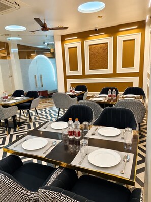 A hotel dining area with tables set for four, equipped with plates, cutlery, and bottled water.