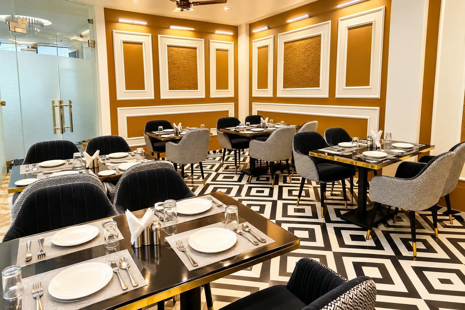 A dining area with tables set for four, chairs upholstered in black and grey, and a patterned floor.