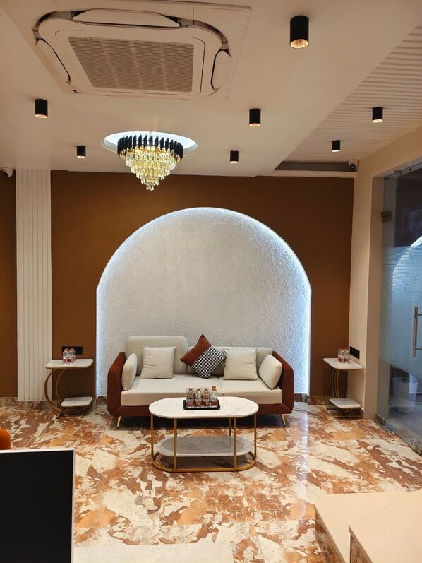 A modern living room with a large arched wall, a chandelier, and a marble floor.