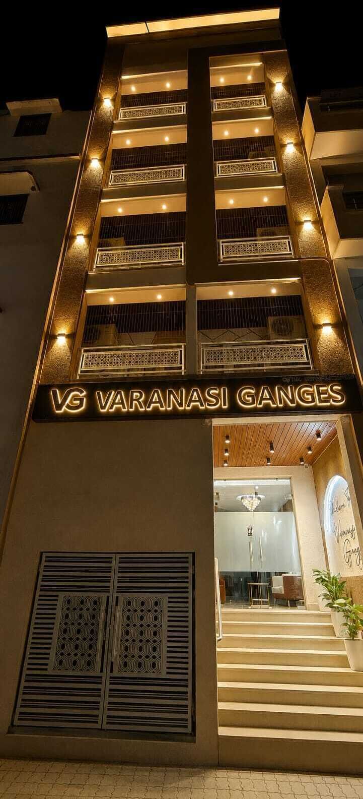 Un edificio con un cartello che recita 'VG Varanasi Ganges' all'ingresso, caratterizzato da un design moderno con finestre illuminate e una scalinata che conduce all'ingresso.