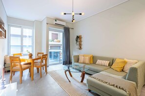 A modern living room with a glass coffee table, a sofa with cushions, a dining area with chairs, and a balcony visible through the window. - Seaside Retreat for Relaxed Kalamata Beach Stays (Kalamata)