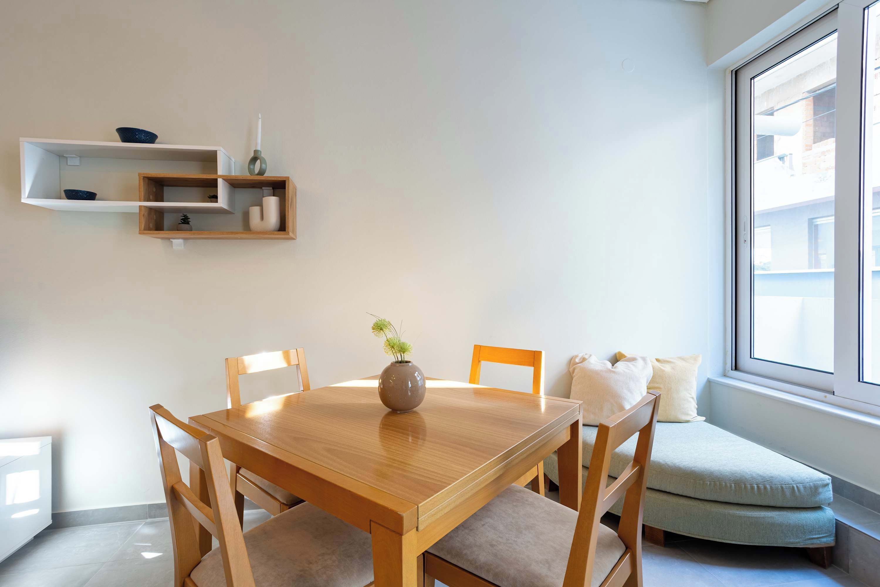Un coin repas comprenant une table en bois, des chaises, un vase avec une plante et un banc intégré agrémenté de coussins.