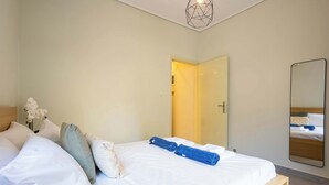 Ein Schlafzimmer mit Bett, Kissen, einem Nachttisch, einem Spiegel und einer Tür zu einem anderen Raum.