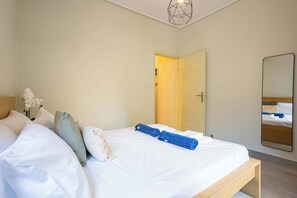 A bedroom with a bed, pillows, a bedside table, a mirror, and a door leading to another room. - Seaside Retreat for Relaxed Kalamata Beach Stays (Kalamata)