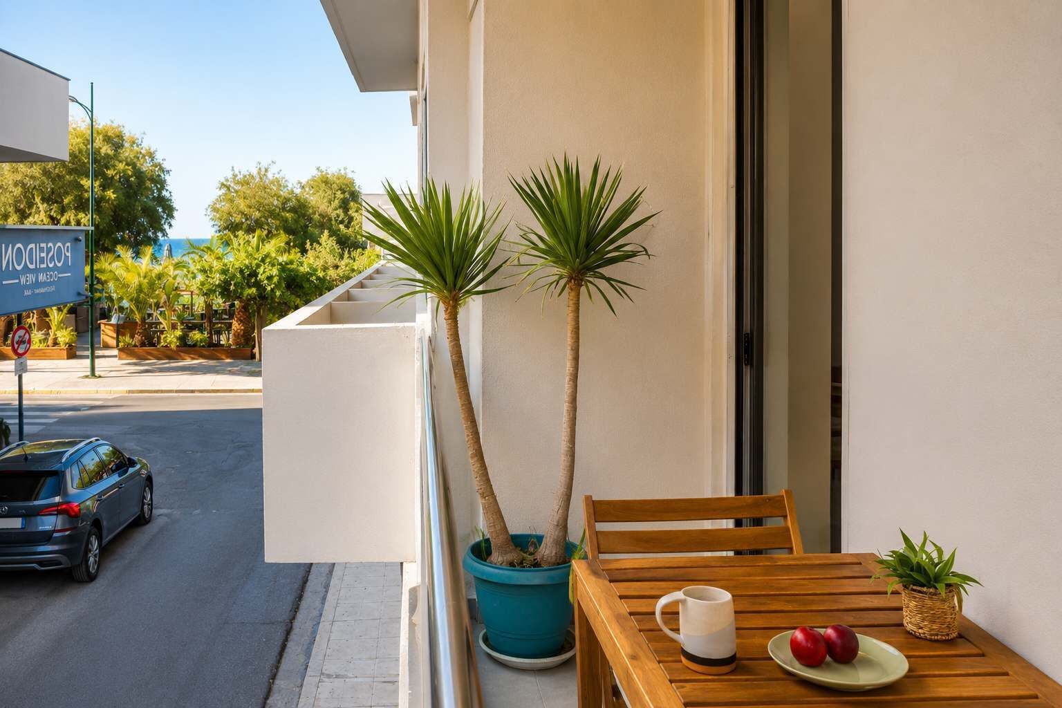 Un balcon avec une table en bois, deux plantes en pot, une tasse et une assiette de fruits.