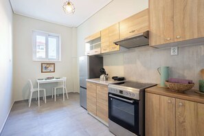 A modern kitchen with wooden cabinets, a stainless steel refrigerator, an oven, and a dining area with a table and chairs. - Seaside Retreat for Relaxed Kalamata Beach Stays (Kalamata)