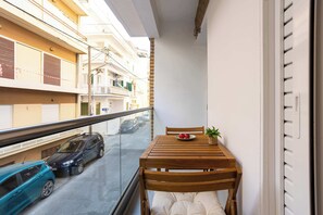 A balcony with a wooden table, a chair, a potted plant, and a bowl of fruit. - Seaside Retreat for Relaxed Kalamata Beach Stays (Kalamata)