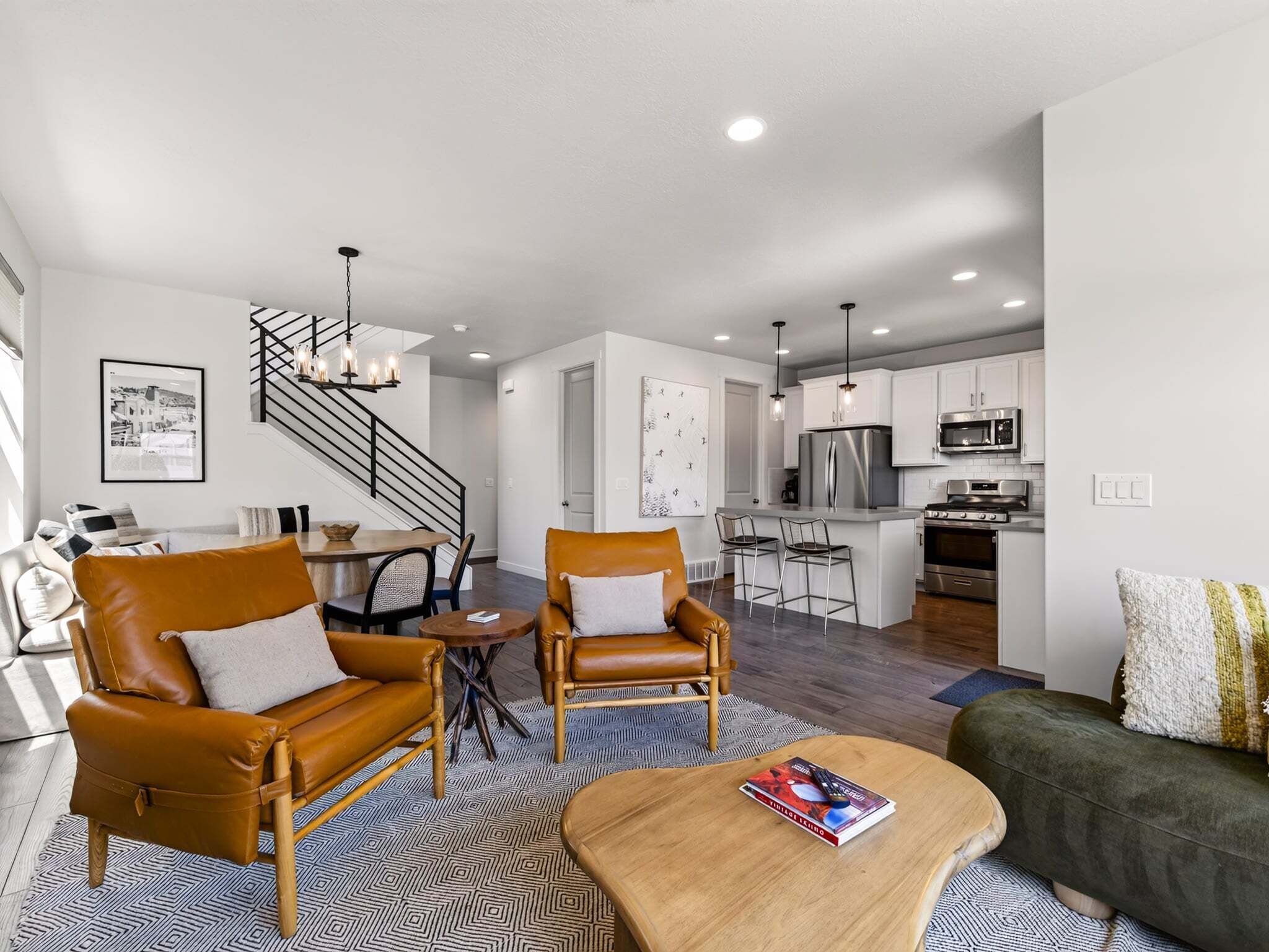 A modern living room with leather sofas, a dining table, and a kitchen area with stainless steel appliances.