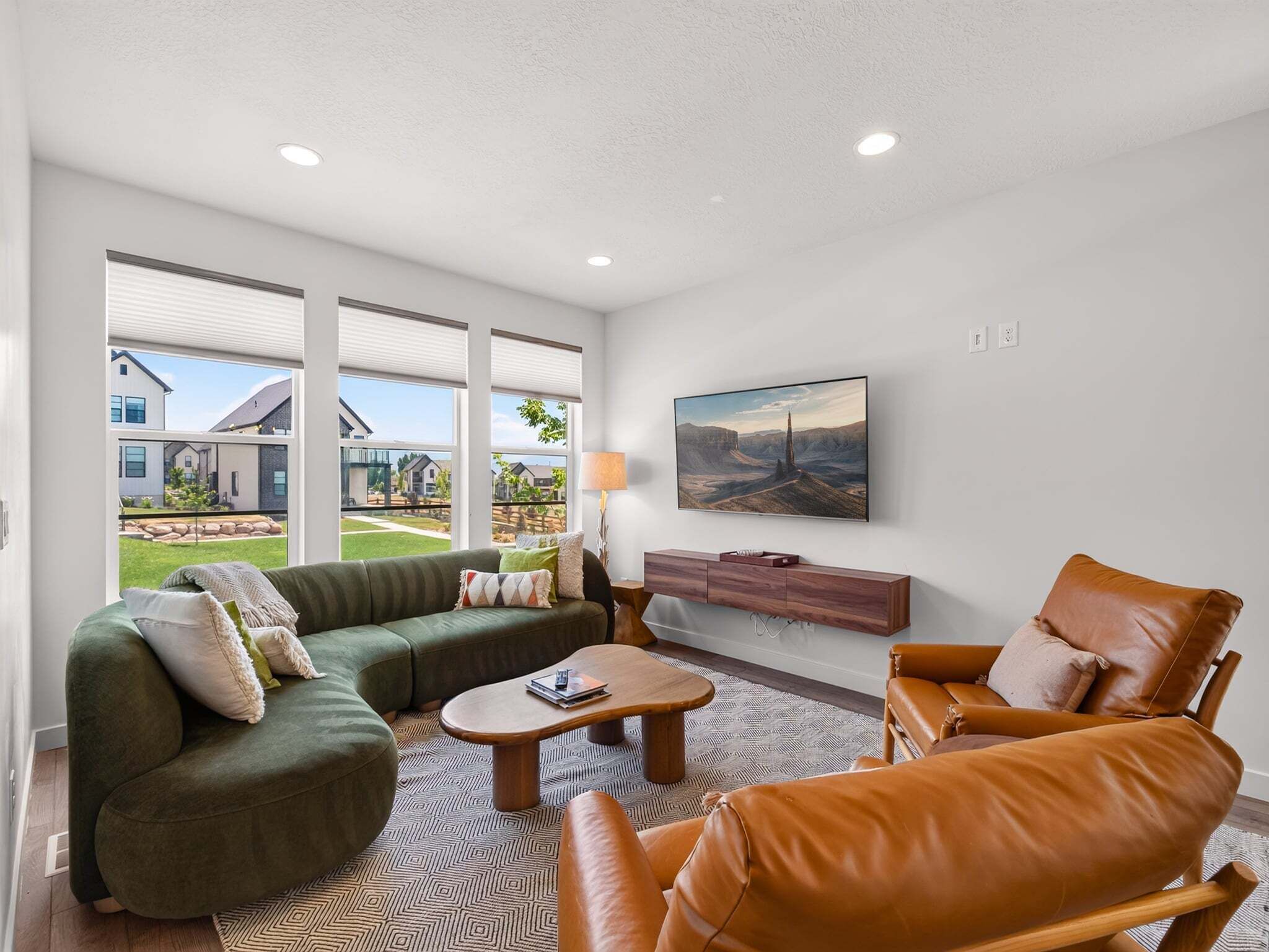 A spacious living room with a sectional sofa, a leather armchair, a coffee table, and a flat-screen TV mounted on the wall.