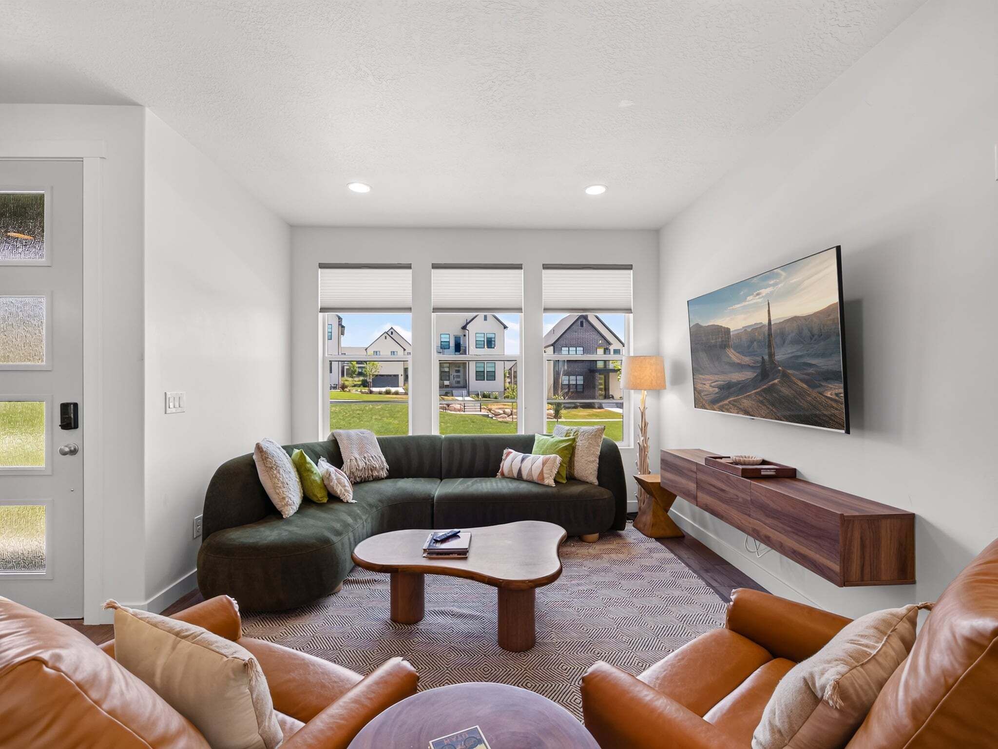 A modern living room with a sectional sofa, leather armchairs, a coffee table, and a large TV mounted on the wall.