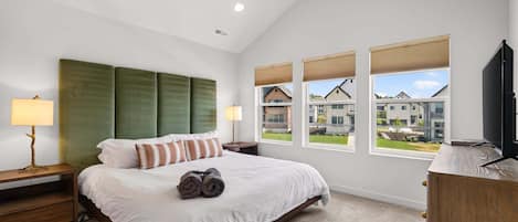 A bedroom with a bed, a ceiling fan, a nightstand, a lamp, a window with a view, and a television.