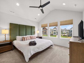 Ein Schlafzimmer mit Bett, Deckenventilator, Nachttisch, Lampe, Fenster mit Blick und Fernseher.