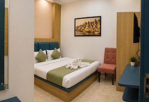 A hotel room with a bed, a chair, a small table, a television, and a wall-mounted picture.
