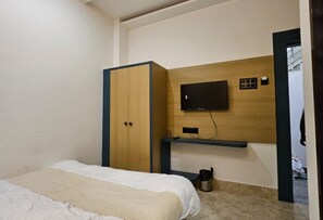 A bedroom with a bed, a wardrobe, a mounted television, and a small shelf.