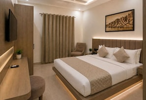 A modern hotel room with a large bed, a desk, a chair, and a television. - New Skyrooms (Varanasi)