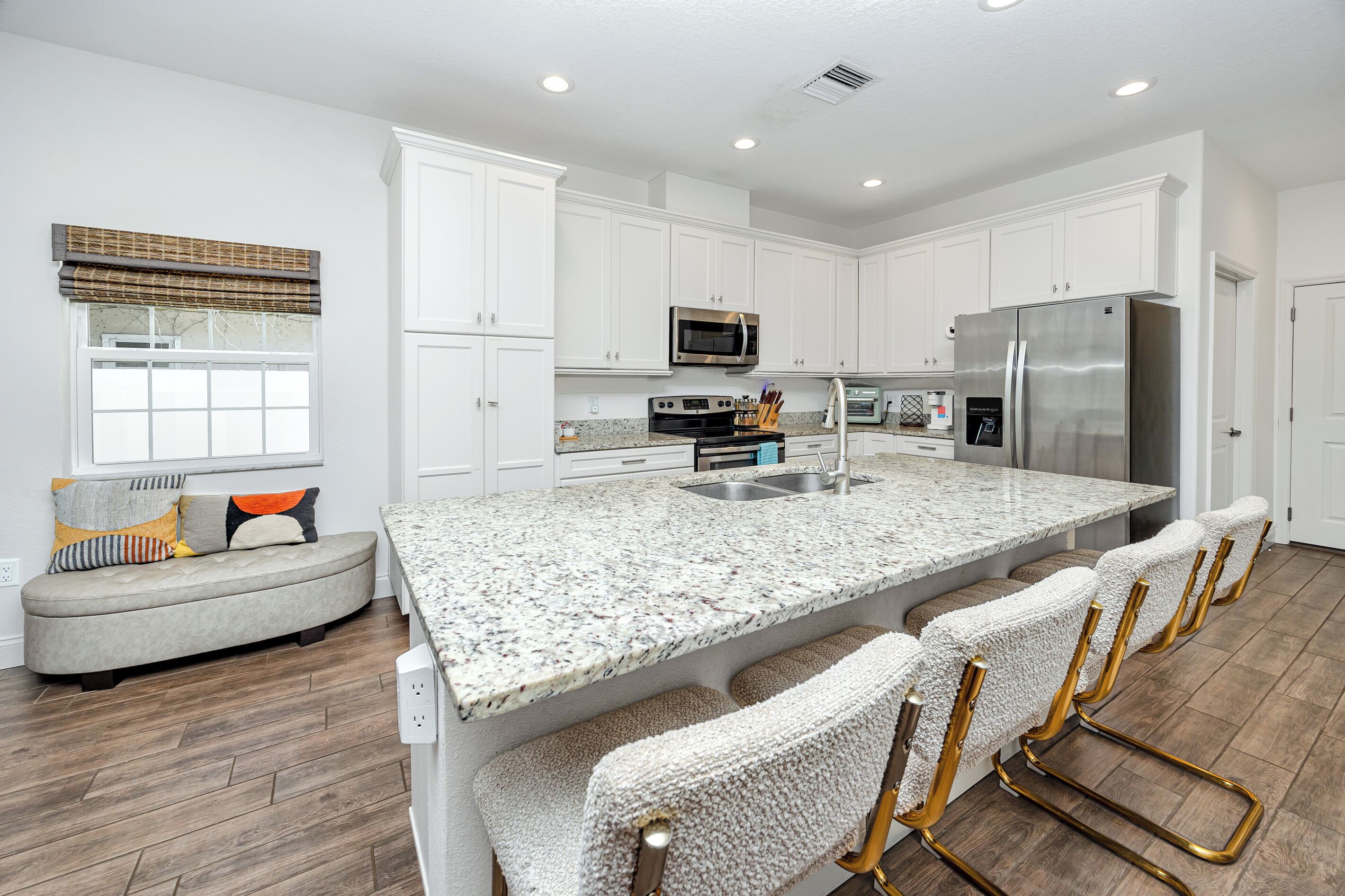 A modern kitchen with white cabinets, a granite countertop, stainless steel appliances, and a built-in bar area.
