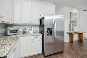 A kitchen with white cabinets, a stainless steel refrigerator, a built-in oven, and a wooden table. - Home Near Belleair Beach (Largo)