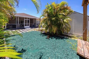 A residential area with a covered patio, a swimming pool with blue tiles, and a wooden deck. - Home Near Belleair Beach (Largo)