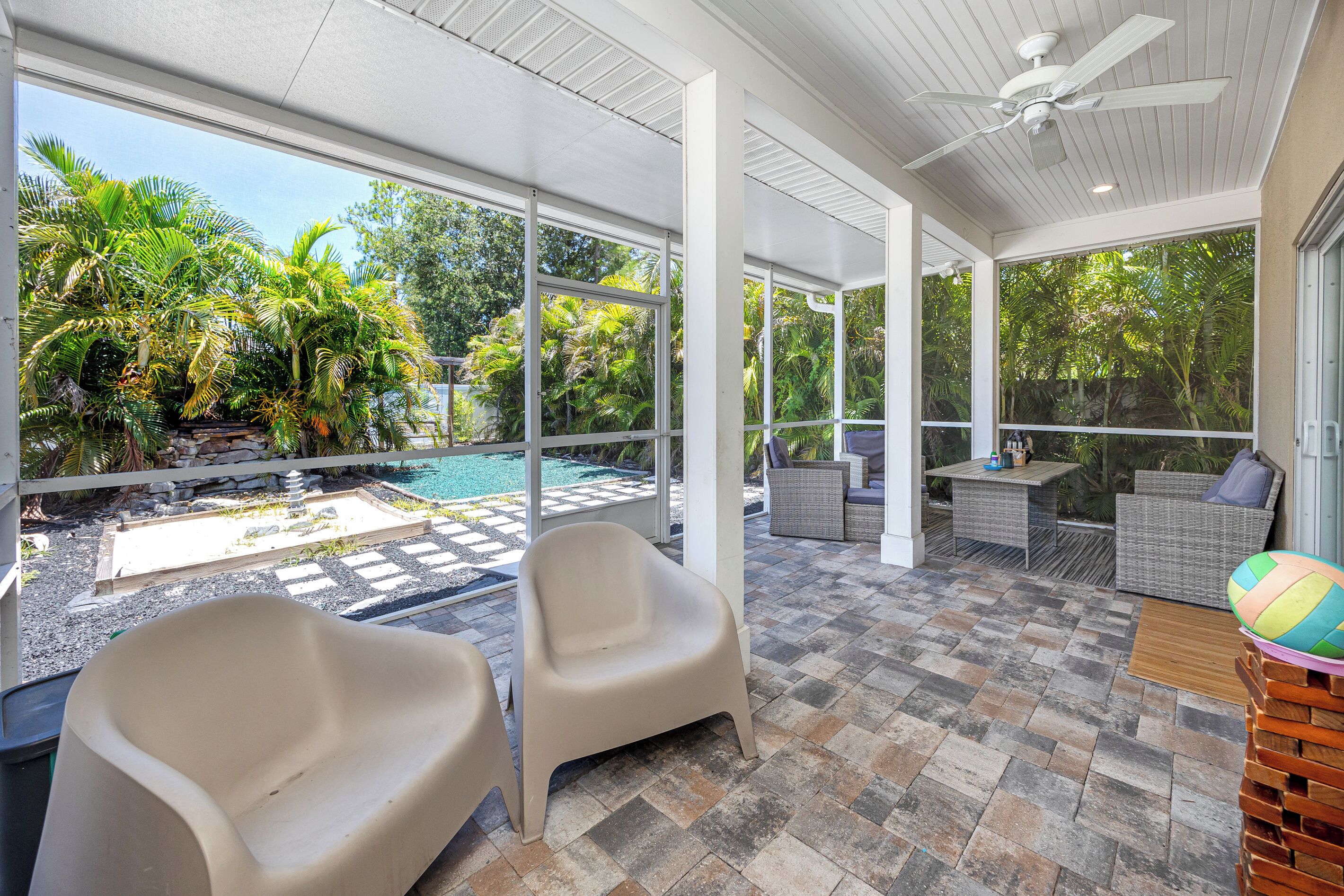 A covered outdoor area with a pool, seating, and a view of greenery.