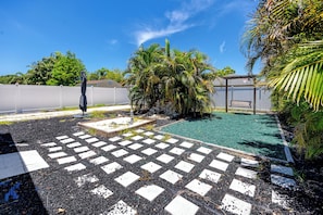 Ein Garten mit Pool, einer Holzterrasse und einem weißen Zaun.