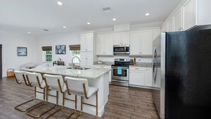 Une cuisine moderne avec des meubles blancs, des appareils en acier inoxydable et un îlot central doté de tabourets de bar.