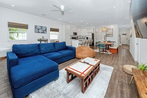 A modern living room with a blue sectional sofa, a coffee table, and a dining area with a table and chairs. - Home Near Belleair Beach (Largo)