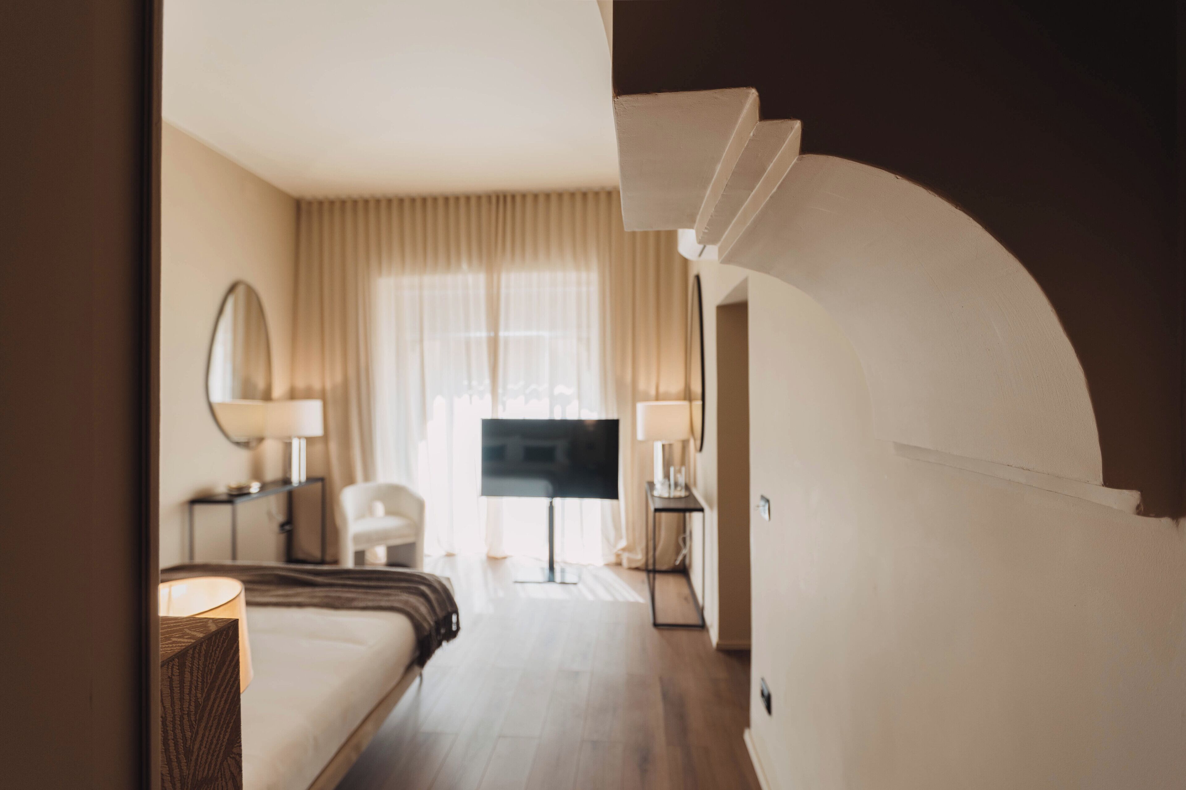 A hotel room with a bed, a desk, a chair, a television, and a window with curtains.