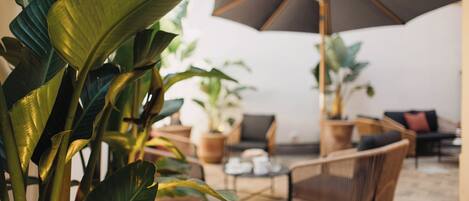 Un área de estar interior acogedora, con una sombrilla grande, plantas en macetas y piso de madera.