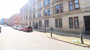A street with parked cars and a row of buildings with large windows and a stone facade. - Glasgow City Escape - 2 Bedroom Apartment (Glasgow)