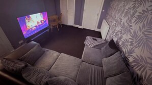 A living room with a flat-screen TV, a sofa, a chair, and a patterned wall. - Glasgow City Escape - 2 Bedroom Apartment (Glasgow)