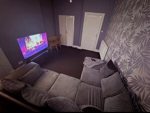 Ein Wohnzimmer mit Flachbildfernseher, einer Couch, einem Sessel und einer Wand mit Muster.