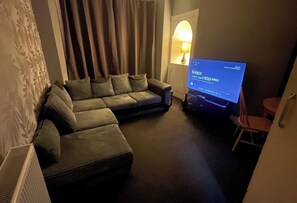 Ein Wohnzimmer mit einer Eckcouch, einem Flachbildfernseher und einer Lampe.