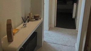A hallway with a white bench, a small table with a candle, and a door leading to another room. - Glasgow City Escape - 2 Bedroom Apartment (Glasgow)