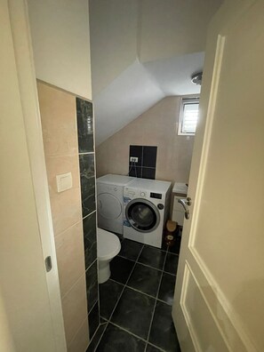 A compact bathroom with a washing machine, toilet, and a small window. - Modern Classic 2-Bedroom Apartment in Donja Lastva (Tivat)